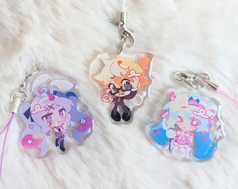 May include: Three clear acrylic charms featuring colorful anime-style character illustrations. Each charm includes a silver-toned metal lobster clasp and a thin cord loop in purple, white, or pink for attachment to personal items or accessories.