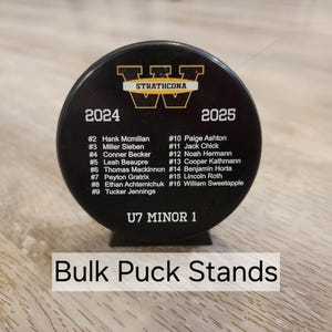 May include: Black hockey puck stand with a white and gold logo that says "Strathcona" and the years "2024" and "2025". The stand has a list of names and numbers for a hockey team. The text at the bottom says "U7 Minor 1".