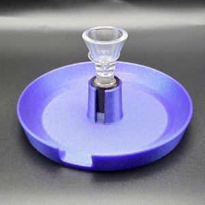 May include: A purple tray with a clear glass bowl and a black base. The tray has a circular design with a cutout on the side. The glass bowl is clear and has a conical shape.