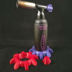May include: A black and silver Big Shot GT 8000 torch with purple accents and a red stand. The torch has a silver nozzle and a purple adjustment knob. Additional red and purple accessories are included.