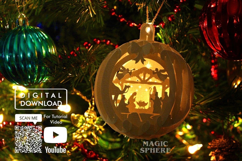May include: A white paper Christmas ornament with a cut-out design of the nativity scene. The ornament is hanging on a Christmas tree with lights and other ornaments.