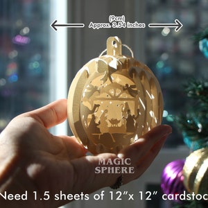 May include: A wooden Christmas ornament with a nativity scene inside. The ornament is 3.54 inches in diameter and requires 1.5 sheets of 12x12 inch cardstock to make. The ornament is labeled "Magic Sphere".