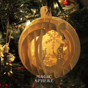 May include: A white paper Christmas ornament with a snowman and snowflake design. The ornament is a 3D paper sphere with the words "Magic Sphere" printed on the bottom.