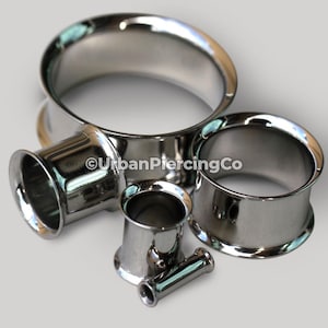 May include: Four silver metal ear gauges of different sizes. The gauges are smooth and shiny. The largest gauge is 1 inch in diameter.