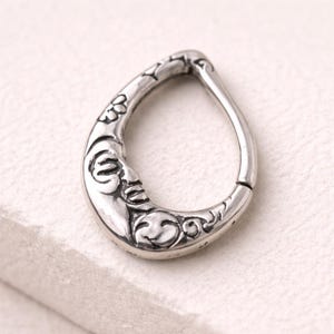 Puede incluir: Pendiente plateado en forma de lágrima con un diseño detallado de luna creciente y floral. El pendiente presenta una cara de luna sonriente y remolinos decorativos.