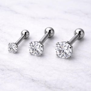 May include: Three silver-colored stud earrings with clear, sparkling round-cut cubic zirconia stones. The earrings are displayed on a white surface. The earrings have a post and ball backing.