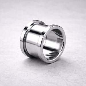 May include: A polished, silver-colored ear tunnel plug. The plug has a cylindrical shape with a flared edge on each end. The surface is smooth and reflective, with a bright, metallic sheen. The design is simple and modern.