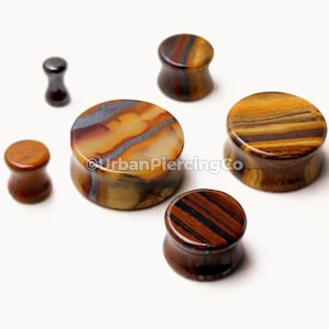 May include: Set of six stone ear gauges in various sizes. The gauges are made of tiger eye, a brown and gold stone with a striped pattern. The gauges are round and have a smooth finish.