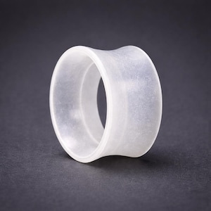 May include: A translucent, white ear gauge plug with a flared design. The plug has a smooth, slightly textured surface and a hollow center. The image is set against a dark gray background, highlighting the plug's shape and material.