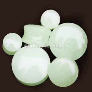 May include: A set of six white jade ear gauges in various sizes. The gauges are smooth and polished, with a subtle green hue.
