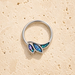 Puede incluir: Un anillo circular de tono plateado que presenta un segmento decorativo con tres incrustaciones en forma de hoja. Cada incrustación contiene material de concha de abulón iridiscente que muestra tonos cambiantes de azul, verde y morado.