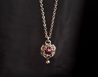Colgante pequeño de malla metálica con una perla roja de agua dulce.
