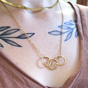 May include: A gold chain necklace with three interlocking circles pendant. The necklace is layered over a thin gold chain.