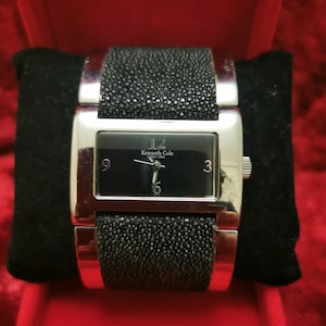 May include: A silver Kenneth Cole New York watch with a black face and black textured band.