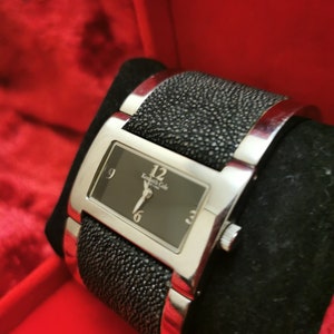 May include: A silver watch with a black face and black leather band. The watch face has silver hands and Roman numeral markings. The band has a textured, alligator-like pattern.