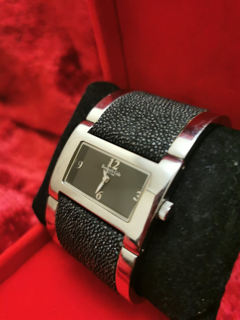 May include: A silver watch with a black face and black leather band. The watch face has silver hands and Roman numeral markings. The band has a textured, alligator-like pattern.