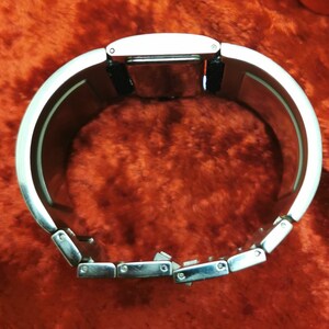 May include: A silver bracelet watch with a black band. The watch has a rectangular face and a silver metal band with a clasp.