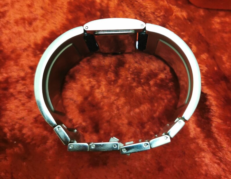 May include: A silver bracelet watch with a black band. The watch has a rectangular face and a silver metal band with a clasp.