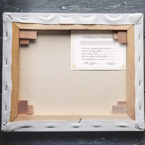 May include: The back of a stretched canvas painting with a Certificate of Authenticity attached. The certificate is for a "Short Beach Scene" painting by "Sandy Stern" and is dated 12/20/2021.