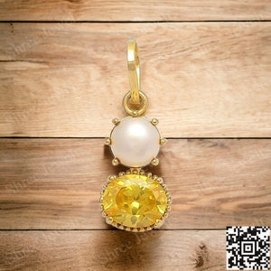 May include: A gold pendant featuring a yellow gemstone and a white pearl. The pendant is displayed against a wooden backdrop.