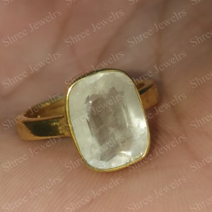 Könnte beinhalten: Ein goldener Ring mit einem klaren, rechteckigen Edelstein. Der Ring ist mit einem großen, facettierten Stein besetzt, der wie ein weißer Saphir aussieht.