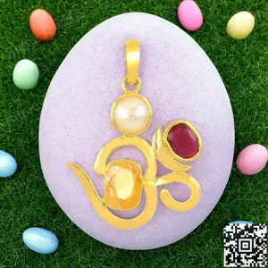 May include: Gold pendant featuring the Om symbol with a white pearl, a yellow gemstone, and a red gemstone.