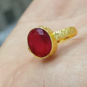 Könnte beinhalten: Ein goldener Ring mit einem roten Edelstein. Der Ring hat eine strukturierte Band.