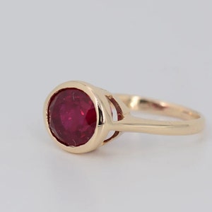 May include: A gold ring with a red ruby gemstone. The ring has a simple design with a bezel setting for the ruby.