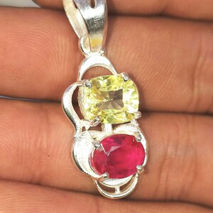 May include: A silver pendant with a yellow and red gemstone. The pendant is in the shape of a heart with a loop at the top for attaching to a chain.