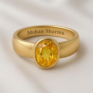 May include: A gold ring featuring a large, oval yellow gemstone. The ring band is engraved with the name "Mohan Sharma". The ring has a simple, elegant design with a polished finish.