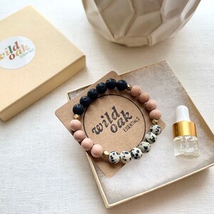 May include: A small gift box with a black and white speckled bracelet, a small bottle of essential oil, and a card with the text "wild oak essentials".