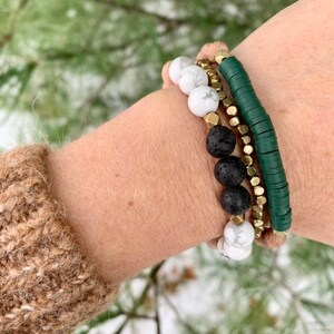 May include: A set of four bracelets featuring green, black, and white beads. The bracelets are made of lava rock, white howlite, and gold-toned metal beads.