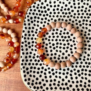 May include: A wooden and carnelian gemstone bracelet on a black and white polka dot tray. The bracelet is made of natural wood beads and carnelian gemstones in shades of orange, red, and yellow.