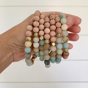 May include: A stack of bracelets with wooden and light blue beads, accented with gold metal beads.