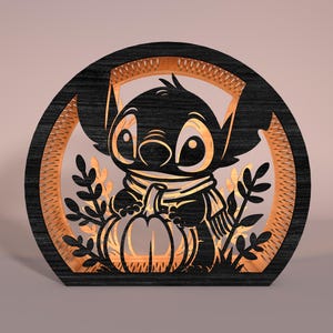 May include: A wooden, layered decoration featuring a black silhouette of Stitch from Lilo & Stitch holding a pumpkin. The design is set within a circular frame with a light-colored interior and leaf accents, perfect for fall.