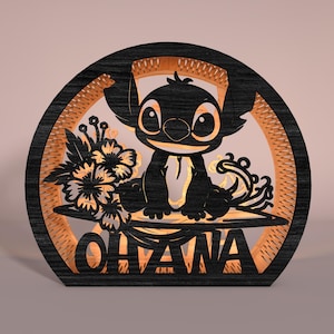 May include: A black and brown wooden decorative piece featuring a cartoon character with large eyes, sitting in front of a floral arrangement. The word "OHANA" is displayed at the bottom of the piece.