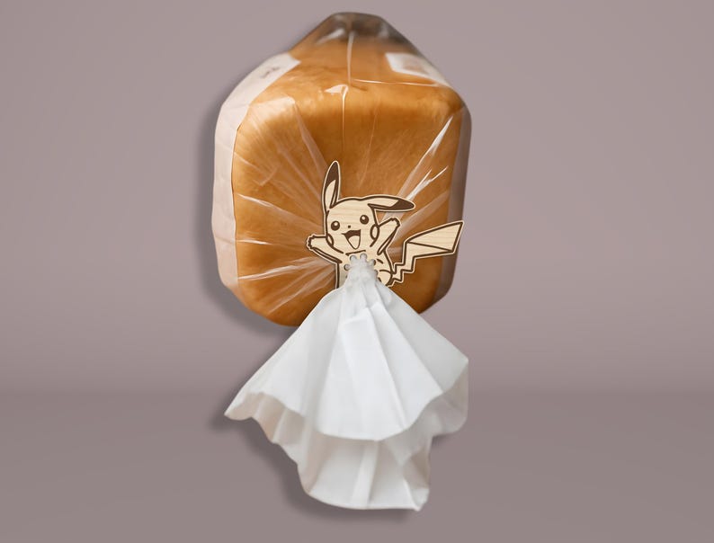 May include: A loaf of bread in a clear plastic bag, with a wooden Pikachu character attached. The bread is light brown, and the bag is sealed with a white paper element.