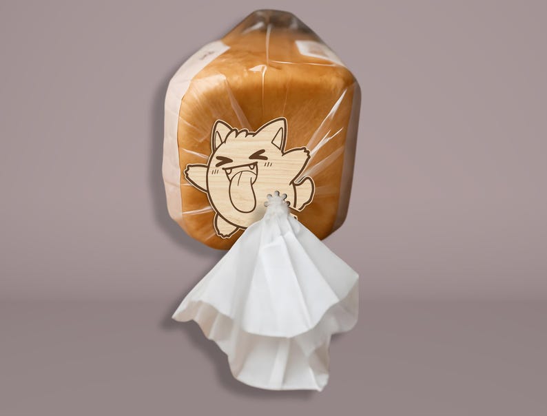 May include: A loaf of bread in a clear plastic bag, secured with a white twist tie. A wooden cat-shaped tag with a tongue sticking out is attached to the bag. The bread is golden brown.
