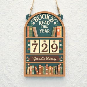May include: Wooden bookshelf-shaped sign with the text "BOOKS READ THIS YEAR" and the number "729". The sign has a teal background with floral and book illustrations. The name "Gabrielle Library" is also displayed.