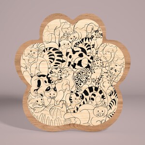 May include: A wooden paw-shaped plaque with a black and white line drawing of a group of cats. The cats are in various poses, some are curled up, some are sitting, and some are standing. The plaque is a light brown color and has a smooth finish.