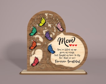 May include: Wooden heart-shaped sign with a tree and butterflies in rainbow colors. The sign reads "Mom You've lifted us up, given us wings, And taught us how to fly. For that we are Forever Grateful".