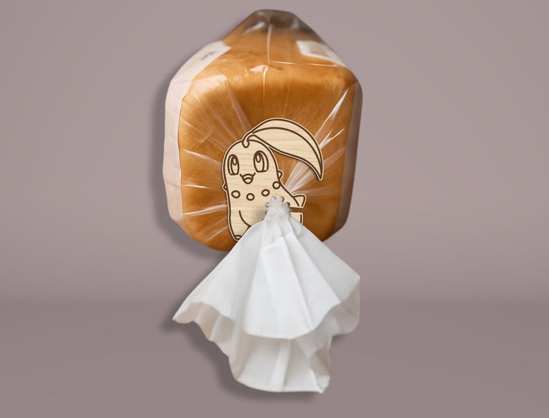 May include: A loaf of bread in a clear plastic bag, sealed with a white paper tie. The bag has a wooden tag with a cartoon character design. The bread is golden brown.