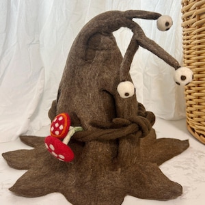 May include: A whimsical brown felt hat with two long, curved antennae, each tipped with a white and brown ball. A pair of red and white mushroom accents adorn the front. The hat has a star-shaped base.