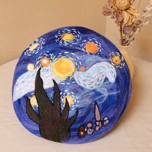 Könnte beinhalten: Eine blaue Filzberet mit einem handgemalten Design, inspiriert von Vincent van Goghs "Sternennacht". Die Beret zeigt einen wirbelnden Himmel mit gelben Sternen, einem schwarzen Baum und einer weißen Wolke.