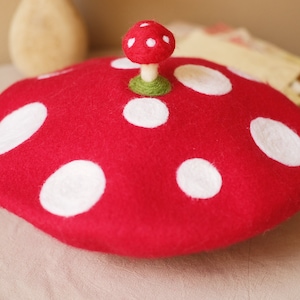 Może przedstawiać: Czerwony kapelusz w kształcie grzyba z białymi kropkami i małym grzybem na górze. Kapelusz to fantazyjny dodatek, idealny na kostiumy lub imprezy tematyczne. Grzyb ma czerwony kapelusz z białymi kropkami i zieloną łodygę.