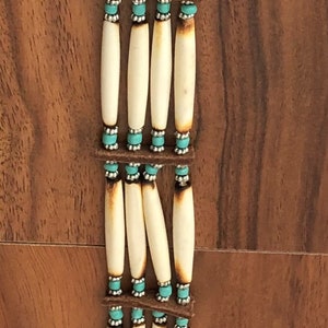 May include: A multi-strand leather bracelet with white bone beads and turquoise accents. The bracelet has a brown leather strap with a knot at the end.