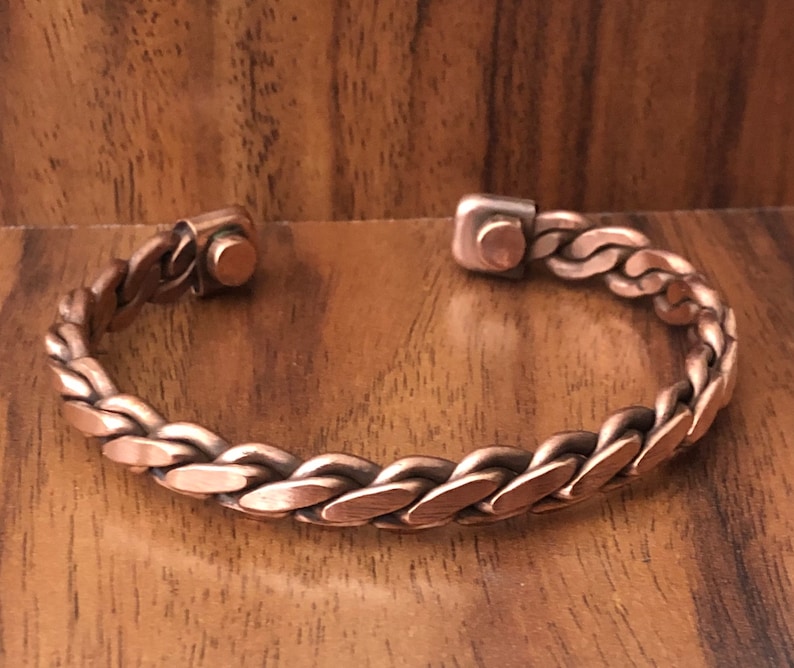 May include: A copper braided bracelet with magnetic clasps. The bracelet is made of a thick, braided copper wire and has a simple, elegant design.