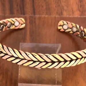 May include: A braided copper bracelet with three different colored metals. The bracelet is open and has a magnetic clasp.
