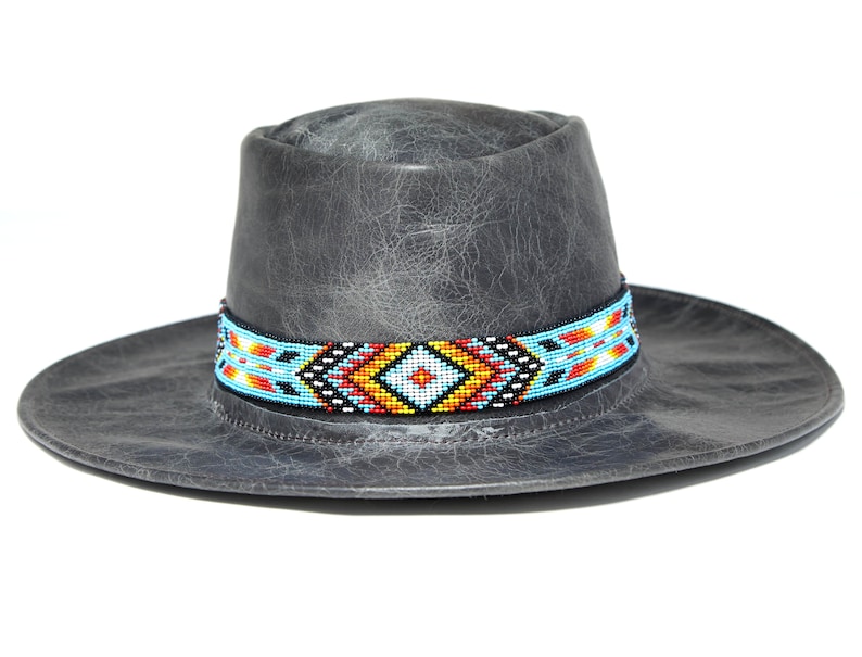Peut inclure: Un chapeau de cowboy en cuir gris avec un bandeau perl&eacute; pr&eacute;sentant un motif g&eacute;om&eacute;trique dans des tons de bleu, rouge, jaune et blanc.