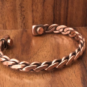 May include: A copper braided bracelet with a magnetic clasp. The bracelet is made of a thick, woven copper wire.